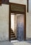 Wooden aged decorated door and beige plaster wall leading to stone staircase