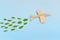 Wooden airplane model emitting fresh green leaves on blue background. Sustainable travel; clean and green energy; and biofuel