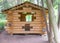 Wooden arbor made of logs with a triangular roof and windows cut into logs.