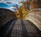 Wooden arch bridge leading into autumnal forestry.