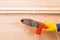 On a wooden background, the hand of a craftsman in yellow gloves, holds a soldering iron for repairing polypropylene water pipes