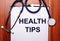 On a wooden background lies a stethoscope and a sheet of paper with the inscription HEALTH TIPS. Flat lay. Medical concept