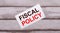 On a wooden background, there is a white card with red text FISCAL POLICY
