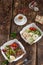 On a wooden background, two vegetable dishes with chicken in a paper box next to a Cup of coffee