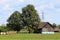 Wooden barn with dilapidated wooden boards next to rows of hay bales wrapped in nylon protection for preservation and tall trees