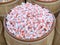 A wooden barrel full of large quantity of wrapped strawberry flavored taffy