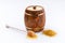 A wooden barrel of honey and a wooden spoon with a drop of tasty liquid and a scattering of pollen on a white background. Close-up
