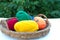 In a wooden basket, against a background of green foliage, there are colored skeins of woolen thread for knitting, next