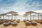 Wooden beach loungers with soft cushions and straw sun umbrellas right on the sea in a tourist resort in Greece against a cloudy