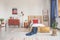 Wooden bed with white bedding and red pillow in spacious bedroom with striped carpet and retro furniture, real photo