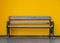 Wooden bench, black iron legs with yellow wall background