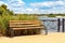 A wooden bench on the Dnipro embankment against the background of tall grass, a wide river of light cloudy sky