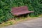 Wooden bench embedded inside the green plants and ivy near the pathway made of asphalt.