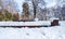 Wooden bench and garbage or junk can on the street or in the park covered with snow in the winter season in trees shadows