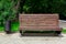 A wooden bench made of brown boards on the back and an iron black litter bin.