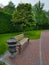 Wooden bench with metal elements in the park. In the background a tree and a tall green hedge from the bush Autumn landscaping