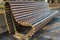 Wooden bench with metal sides that have the shape of heart that laid on one side, standing on stone sidewalk in front of curb