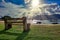 Wooden bench and stone by the sea at incredible sunset with sun rays passing between clouds and boats in the background in Ilhabel