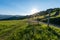 A wooden bench with a wooden cross in the green meadows with mountains and the rising sun in the background Romania