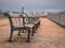 Wooden benches aligned in line on the pier with boats at the background