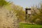 Wooden big raised hunting blind standing on meadow amidst blooming trees and white blooming shrubbery in early spring