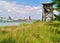 Wooden bird watch tower and port with commercial ships  and cranes. Grass and sky with clouds