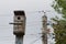 Wooden birdhouse weighs on a wooden post with electric wires in the countryside.