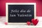 Wooden blackboard with red hearts and written sentence in Spanish Feliz dia de San Valentin, which means Happy Valentine`s day