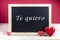 Wooden blackboard with red hearts and written sentence in Spanish Te quiero, which means I love you
