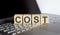 Wooden blocks with COST text of concept on the laptop