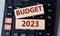 Wooden blocks with the text BUDGET 2023 lie on a black calculator on a gray background