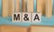 Wooden blocks with text M and A on light blue paper, business concept. MA - short for mergers and acquisitions