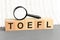 On wooden blocks under a magnifying glass text: toefl. Educational concept. TOEFL - words from wooden blocks with letters, Test of