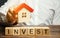 Wooden blocks with the word Invest and house in the hands of a businessman. The concept of investing in real estate construction.