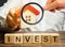 Wooden blocks with the word Invest and house in the hands of a businessman. The concept of investing in real estate construction.