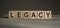 A wooden blocks  with the word LEGACY written on it on a gray background