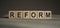 A wooden blocks with the word REFORM written on it on a gray background
