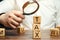 Wooden blocks with the word Tax and a magnifying glass in the hands of a businessman. The concept of studying the size of taxes.