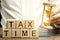 Wooden blocks with the word Tax time and taxpayer with a hourglass. The concept of paying the tax rate. Taxation / burden. Pay off