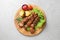 Wooden board with barbecued meat, garnish and sauce on grey background