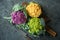 Wooden board with colorful cauliflowers on dark table