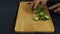 On a wooden Board, cut a green cucumber in large round parts. Strong hands, sharp knife. There is a tablecloth on the table. woman