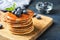 Wooden board with pancakes, syrup and blueberries on table