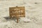 Wooden board stuck in the sand with text ENJOY SUMMER LOST IN PARADISE