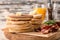 Wooden board with tasty pancakes, butter and fried bacon on table, closeup