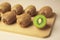 Wooden board with whole kiwis and cut one on beige background, closeup