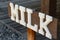 Wooden board with word milk. Signboard with directions to buy milk. White Milk writing with letters on dark background