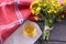 On a wooden boards lies a tablecloth next to a bouquet of rapeseed and a cup with rapeseed oil