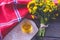 On a wooden boards lies a tablecloth next to a bouquet of rapeseed flowers and a cup with rapeseed oil