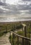 Wooden boardwalk onto a pebble beach in late afternoon light with clouds and sunlight on the ocean.